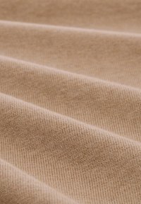 Beige stof die op katoen lijkt met een zachte textuur, voorzien van diagonale ribbels en subtiele variaties in tint over het oppervlak.