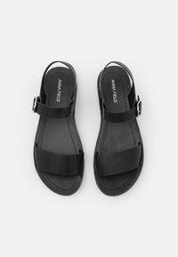 Mustad mustad kahe laia rihmaga, tagarihmaga ja hõbedase klambriga. Sile tekstuur ja minimalistlik disain. Tootja silt on nähtav.
