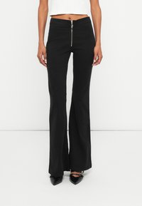 Pantalones negros de campana con un cierre en la parte frontal, hechos de una tela suave. Ajustados en la cintura, presentan un sutil estiramiento y un efecto de campana en el dobladillo.