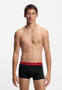 Sorte boxer briefs med en rød elastisk taljebånd med "HUGO" logoen, lavet af et glat stof for en tætsiddende pasform.
