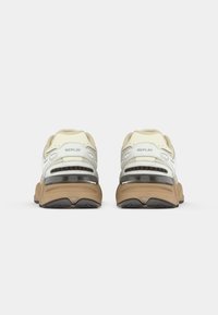 Sport shoes in light tan and white, featuring mesh overlays, a padded collar, and a chunky outsole with grooves for traction.