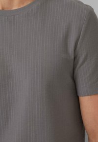 Graues T-Shirt mit kurzen Ärmeln, das ein strukturiertes, feines Rippmuster und einen Rundhalsausschnitt aufweist. Der Stoff wirkt weich und leicht.