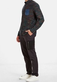 Randig knapp-up skjorta med en blå denim bröstficka, matchad med mörka byxor som har en ficka med dragkedja på sidan och vita sneakers.