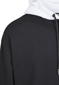 Fekete kapucnis pulóver fehér bélésse. Texturált anyag, húzózsinóros részletek és kontrasztos gallér. Egyszerű dizájn és laza szabás.