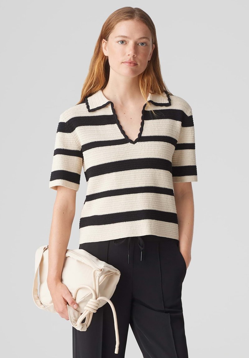 Haut en tricot de style polo avec des rayures horizontales noires et crème, col en coquille, manches courtes et tissu texturé ; associé à un sac beige.