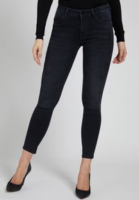 Jeans skinny in denim scuro con un design aderente, styling classico a cinque tasche e una texture sottile. Abbinati a tacchi neri a punta.