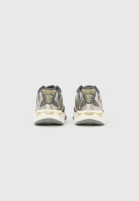 Ζευγάρι γκρι αθλητικών παπουτσιών με λευκές σόλες, ύφασμα από δίχτυ, και κίτρινες λεπτομέρειες λογοτύπου, από μια οπτική γωνία από πίσω σε απλό λευκό φόντο.