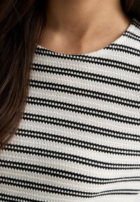 Tissu tricoté à rayures noires et blanches, avec des largeurs de rayures variées et une apparence texturée. Encolure ronde ; sans fermetures ni embellissements visibles.