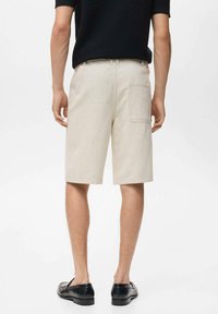 Pantalones cortos de algodón beige con corte recto, detalle de bolsillo trasero y acabado a medida, combinados con zapatos de cuero negros.