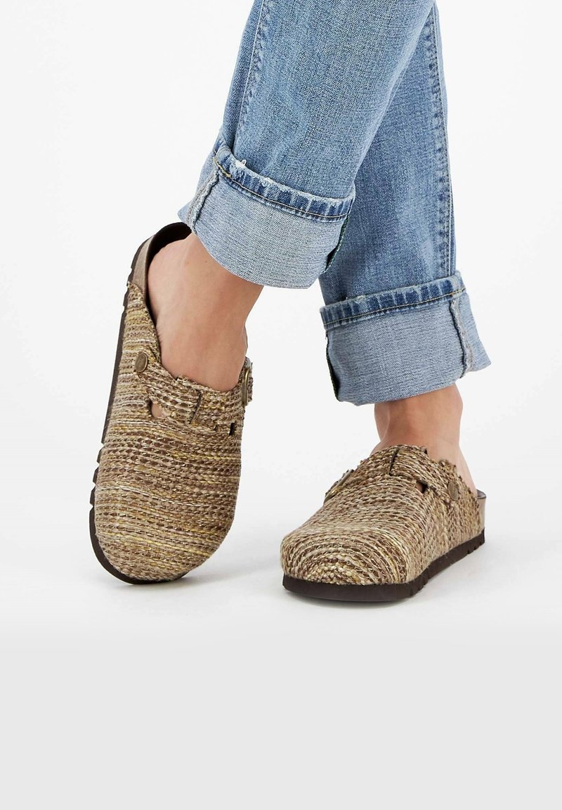 Sabots en paille tissée de couleur marron clair et beige avec un léger talon compensé, dotés d'une sangle à boucle et de découpes.