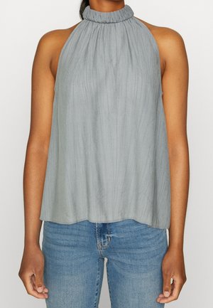 Haut sans manches gris clair à col halter froncé porté avec un jean en denim bleu sur une personne à la peau marron moyenne.