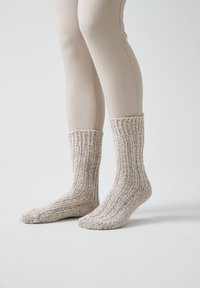 Calcetines de punto con una mezcla de colores beige claro y crema, que presentan una textura acanalada y puños de longitud media, alineados con una superficie suave.