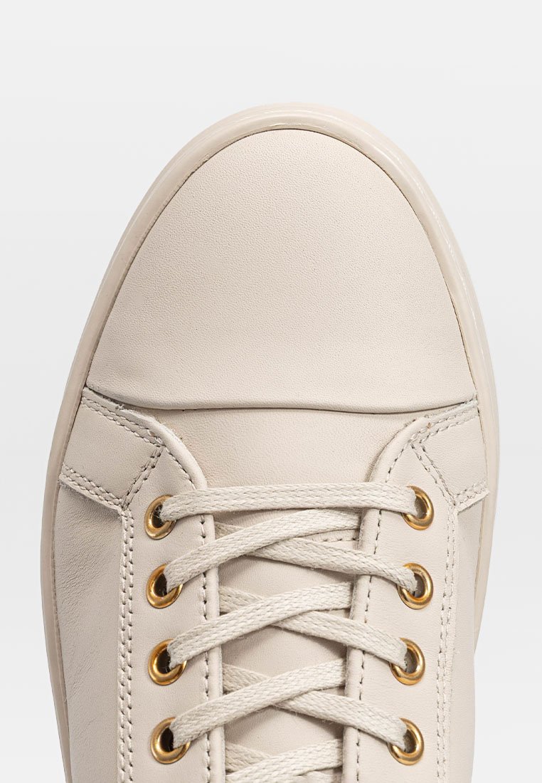 Beżowe skórzane sneakersy z okrągłym noskiem, płaskimi sznurówkami, złotymi oczkami i detalami szycia wzdłuż boków. Całość o gładkiej teksturze.