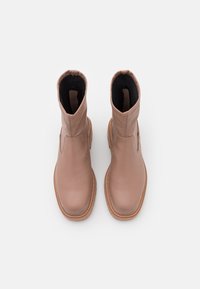 Botines de cuero rosa hasta el tobillo con una textura suave, punta redondeada y paneles laterales elásticos. Presentan un borde cosido y suela de goma.