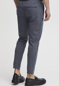 Pantalons gris confort en tissu doux, dotés de deux poches arrière et d'une coupe fuselée, associés à des chaussures noires à enfiler.