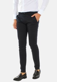 Pantaloni slim-fit blu in un tessuto liscio con chiusura a bottone, caratterizzati da tasche laterali e un taglio su misura, abbinati a mocassini neri.