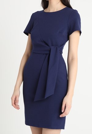 Laivastonsininen mekko, jossa on lyhyet hihat, vartalonmyötäinen siluetti, kietaisumalli ja solmittu vyötärön yksityiskohta. Valmistettu sileästä kankaasta, jossa on siisti viimeistely.