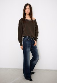 Sötétzöld, vállat szabadon hagyó pulóver ezüst szegecsekkel, laza sötétfarmer nadrággal és fekete, hegyes orrú cipővel párosítva. Egyszerű, hétköznapi stílus.