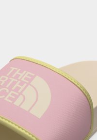 Ροζ και κίτρινο σανδάλι North Face τύπου σαγιονάρα με φαρδιά λουρί που φέρει το λογότυπο της μάρκας, εμφανισμένο σε κοντινή λήψη σε λευκό φόντο.