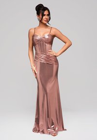Roséguld, figurnära aftonklänning med sweetheart-halsringning, tunna axelremmar och draperad detaljering. Slät, glänsande tyg flödar ner till golvet.