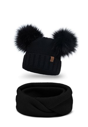 Căciulă tricotată neagră, cu două pomponi din blană neagră și o bandă ribbed. Sub aceasta se află o fular infinity tricotat negru, asortat.
