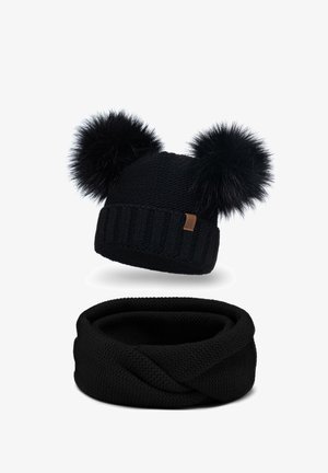 Sort strikket beanie med to sorte pels-pomponer og en ribbet kant. Nedenfor er et matchende sort strikket infinity-sjal.