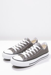 Graue Segeltuch-Sneaker mit weißen Gummisohlen und Zehenkappen. Mit weißen Schnürsenkeln und einem schwarzen Streifen entlang der Sohle. Klassisches Low-Top-Design.