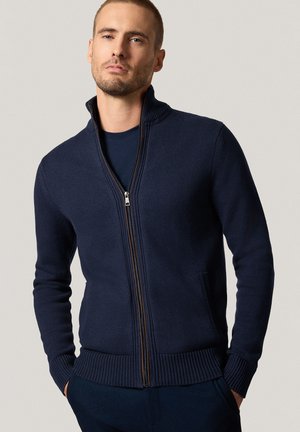 Granatowy sweter zapinany na zamek z teksturowanej tkaniny, z prążkowanymi mankietami i dołem, wyposażony w boczne kieszenie oraz stojący kołnierz.