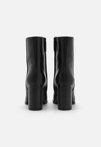 Botas de cuero negras hasta el tobillo con punta cuadrada, tacón grueso y cierre de cremallera lateral, con textura suave y diseño minimalista.