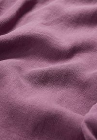  tela de lino en un suave color malva, con una superficie texturizada y suaves pliegues, que muestra las características de la fibra natural.