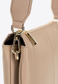 Borsa a mano in pelle beige con finitura testurizzata, dotata di accessori in oro, tracolla removibile e chiusura con zip con charm brandizzato.