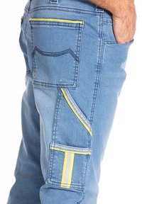 Pantalons cargo en denim bleu avec des coutures jaunes, des poches latérales et une finition texturée. Présente des éléments de design distincts, y compris des rayures contrastées.