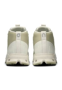 Kõrged spordijalatsid neutraalses kreemjas värvuses, mis on valmistatud siledast sünteetilisest materjalist, tekstureeritud paneelidega ja silmapaistva tabiga seljaosas.