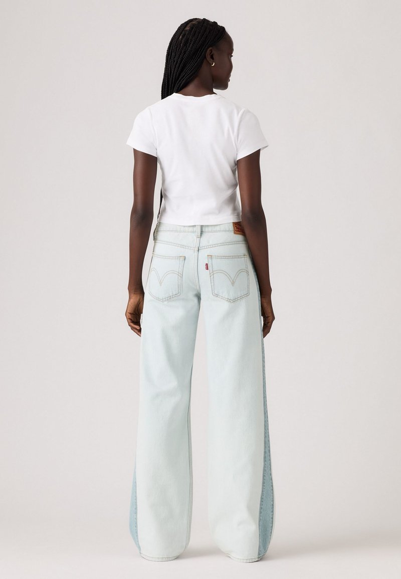 Hellblaue weit geschnittene Jeans mit kontrastierenden Denim-Seitenpaneelen, hoher Taille und zwei Gesäßtaschen mit dem Levi's-Logo. Weißes cropped T-Shirt.