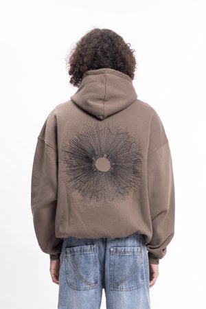 Brauner Kapuzenpullover mit oversized Passform. Auf der Rückseite befindet sich ein schwarzes grafisches Muster, das strahlende Linien ähnelt. Getragen mit hellblauen Jeans.
