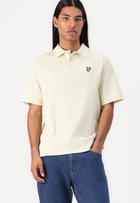 Polo shirt jaune clair avec une finition texturée, doté d'un col et de manches courtes. Comprend un petit logo papillon noir et jaune.