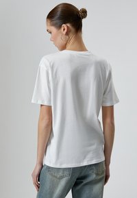 Hvid bomulds t-shirt med korte ærmer og en afslappet pasform, med en rund halsudskæring og en glat tekstur, parret med lyseblå jeans.