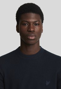 Suéter de color navy con escote redondo, hecho de una tela suave y texturizada. Presenta un logo sutil en el lado izquierdo del pecho.