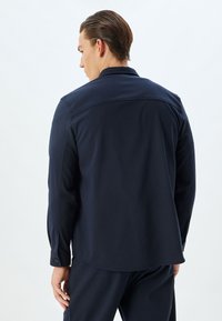 Marineblauw overhemd met lange mouwen en een kraag, met een gladde textuur en knoopmanchetten. Het achteraanzicht toont details van de schoudernaden.