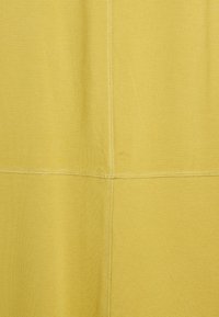 Gelbes Gewebe mit einer glatten Textur, das kontrastierende Nähte entlang der Nähte aufweist und geometrische Muster in einem rechteckigen Layout erzeugt.