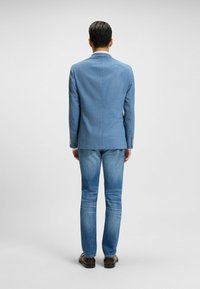 Blå rutad kavaj i kombination med ljusblå jeans. Kavajen har en skräddarsydd passform med slag och diskreta detaljer i metall.