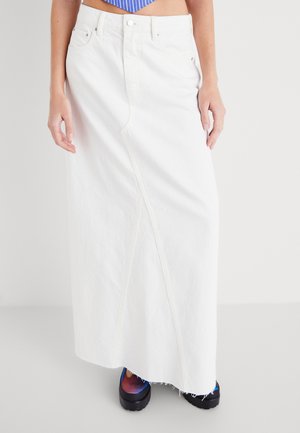 Falda maxi de mezclilla blanca con una abertura frontal, cierre de botón clásico y diseño de cinco bolsillos, combinada con zapatos de plataforma negros.