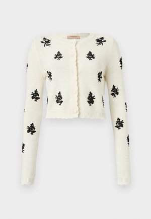 White knitted cardigan featuring black floral embroidery, long sleeves, a cropped fit, and a ruffled button placket.