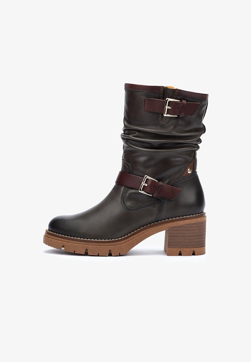 Botín de cuero marrón con un eje arrugado, acentos de hebilla marrones y un tacón de bloque de madera robusto, con una suela texturizada.