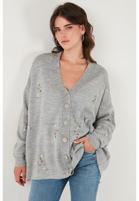 Cárdigan abotonado en gris claro con cuello en V, que presenta bordados florales en azul, amarillo y rojo, y puños acanalados. Textura de punto suave.