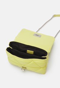 Kulturoidun keltaisen olkalaukun, jossa on hopeinen kiinnitys, ketjuhihna ja musta sisävuori, jossa on etiketti.