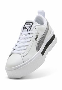 Λευκό αθλητικό παπούτσι Puma με παχιά σόλα, γκρίζα σουέτ λωρίδα, μαύρα λογότυπα Puma στη γλώσσα, το πλάι και τη σόλα, και λευκά κορδόνια.