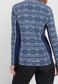 Granatowa i jasnoniebieska bluzka z długim rękawem, wzorzysta, z geometrycznymi motywami, kontrastującymi panelami z boku oraz wysokim kołnierzem.