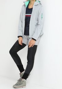 Ljust grå, zip-up jacka med turkos insida, tillsammans med en marinblå skjorta med vita och röda ränder, grå shorts och svarta leggings.