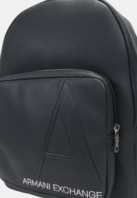 Zaino nero realizzato in vera pelle testurizzata, con una tasca frontale caratterizzata da un design in rilievo della lettera 'A' e una zip argentata. Logo in bianco.